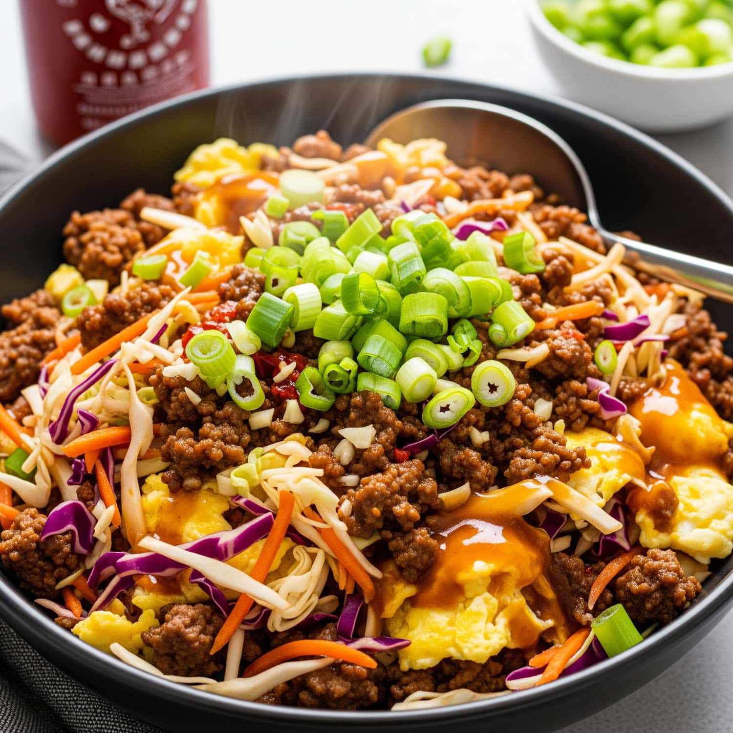 A macro-friendly beef and veggie eggroll low carb in a bowl recipe with lean ground beef, cabbage slaw, and scrambled egg whites, drizzled with sriracha.